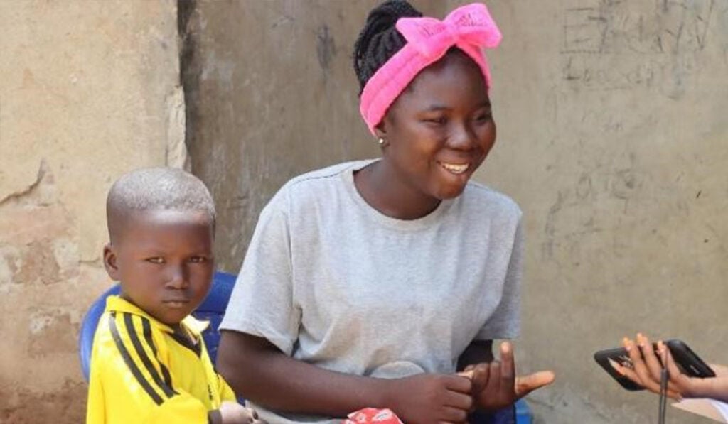 Faith sits, smiling, with her son by her side.