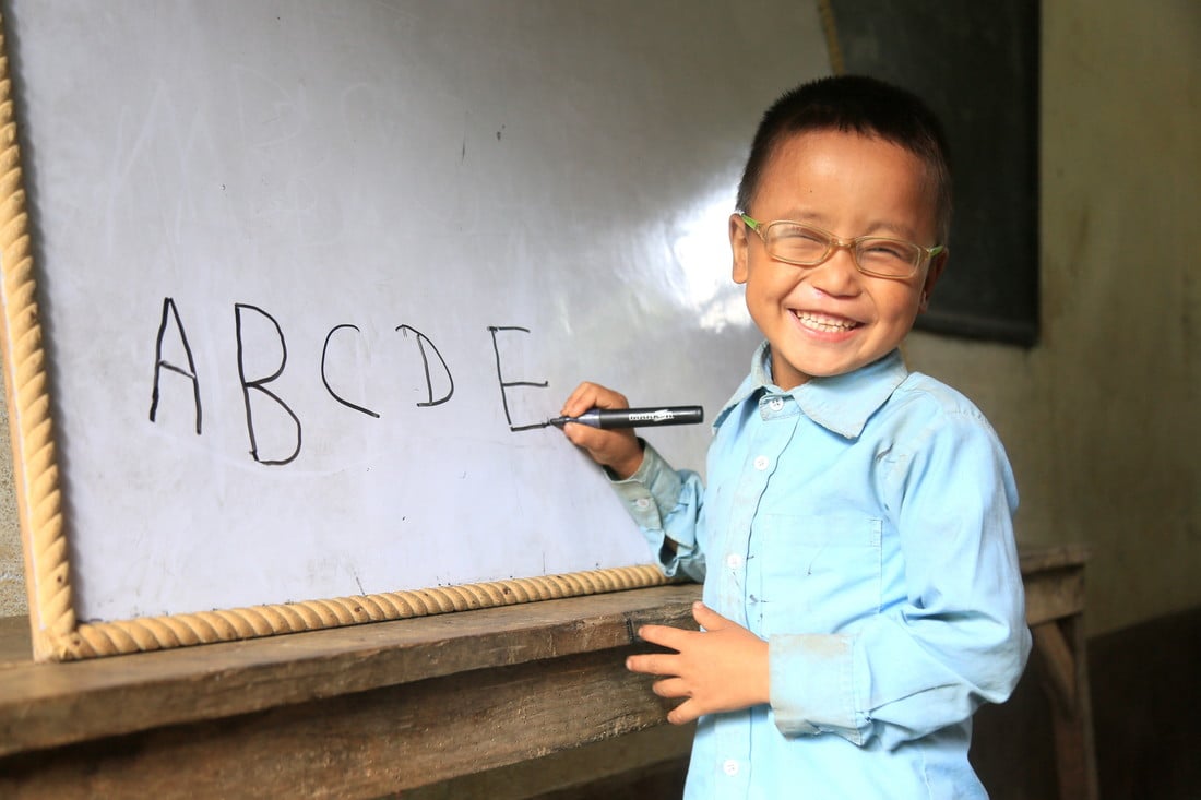 Sudip standing next to a whiteboard in school, with the letters A B C D E written on the board.