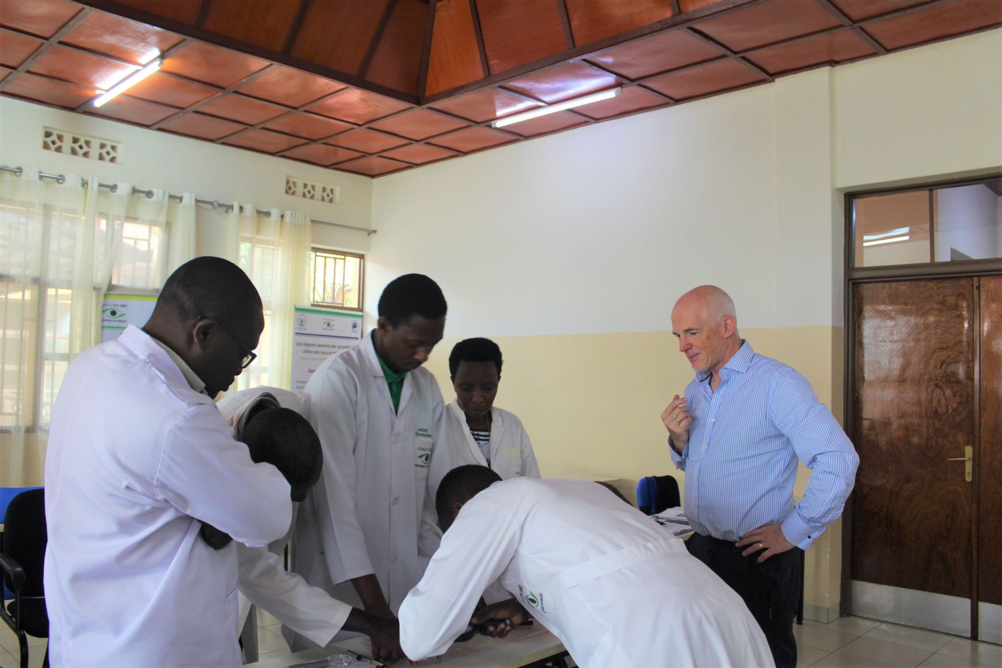 Jonathan Jackson and participants from the training standing in a group looking a low vision instrument on the table,.