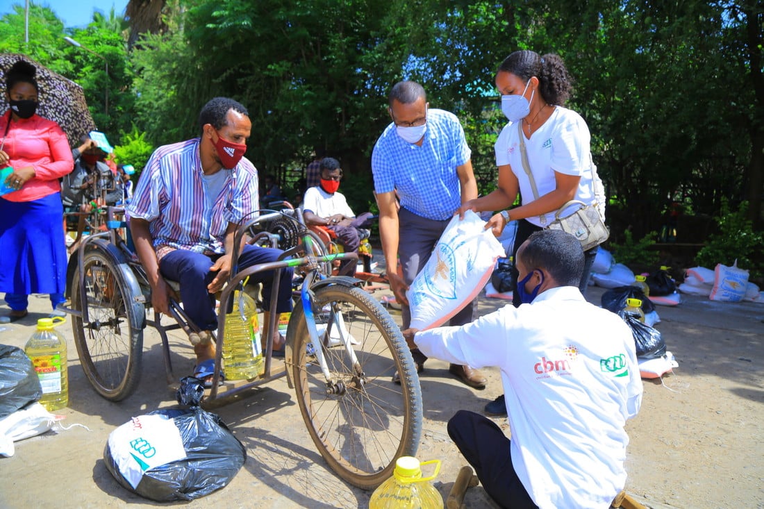 Man with a physical disability on a tricycle being handed food parcels by staff wearing face masks