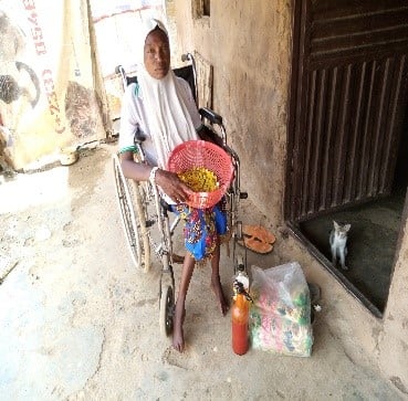 Wheelchair user, Amina, in front of her house, displaying the items she sells. 