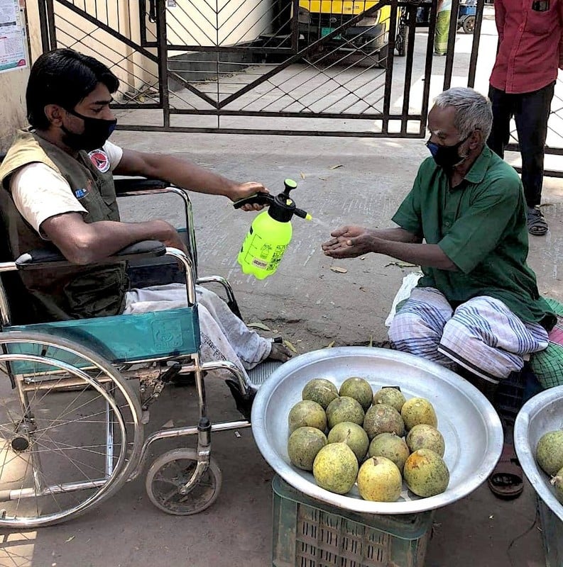 Roman, 32, from Bangladesh sitting in a wheelchair spraying antibacterial gel on a recipient hands
