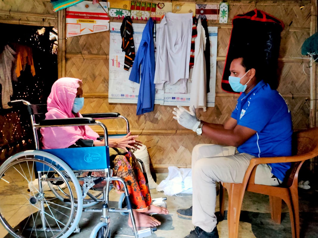 Elderly lady in a wheelchair wearing a face mask and talking to a man wearing a face mask