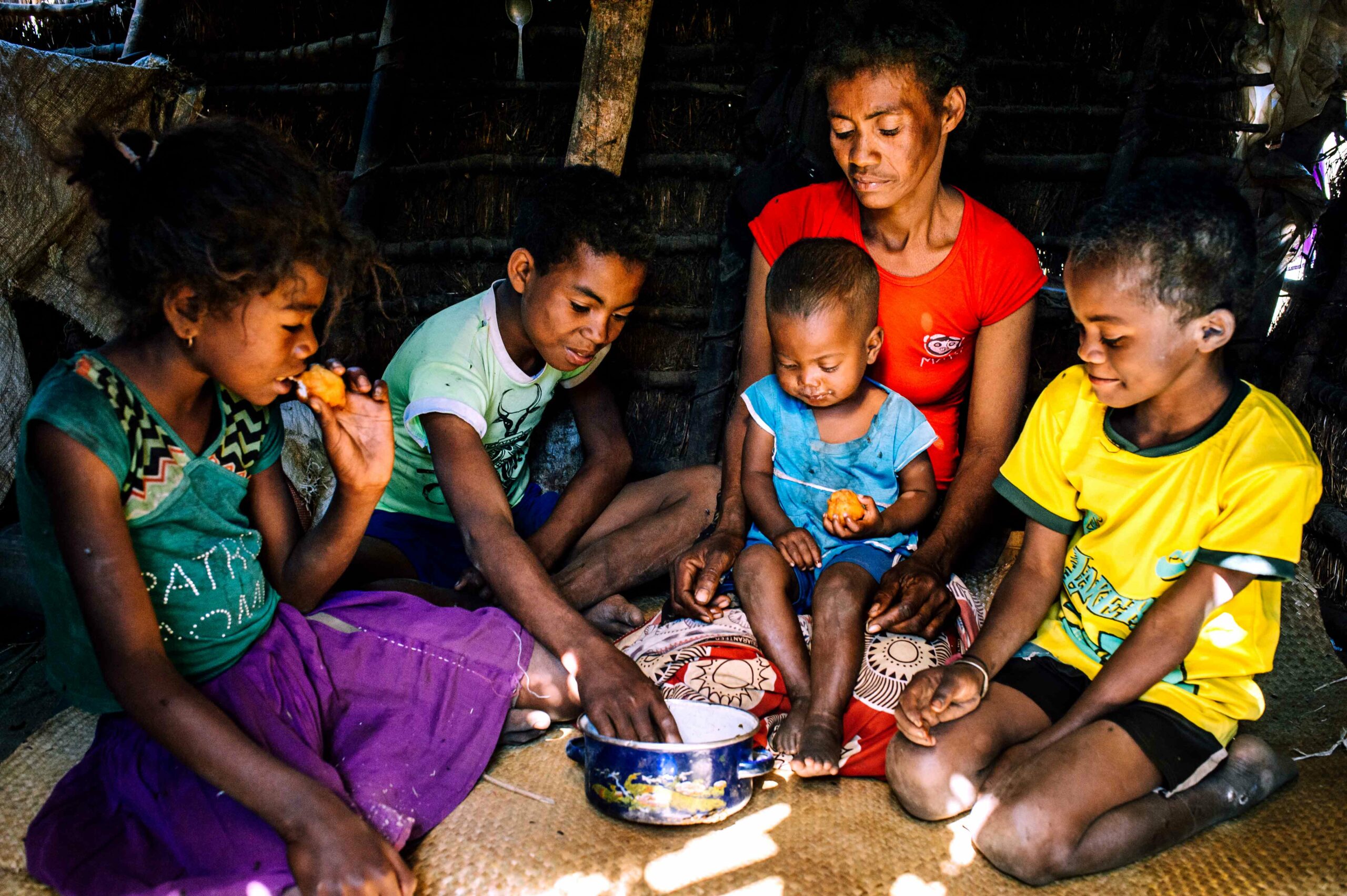 Family sitting on the floor of their house eating from one pot of food