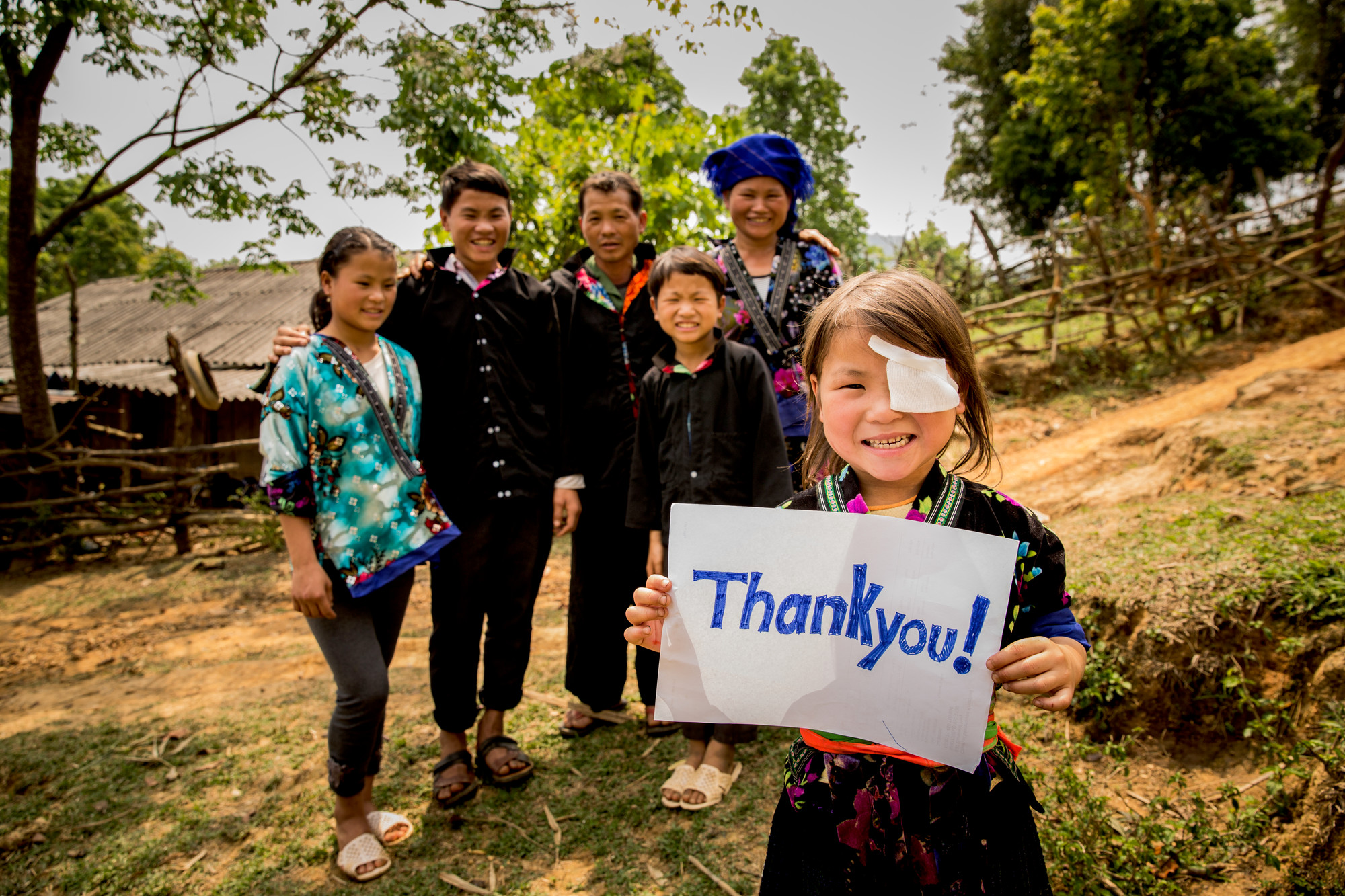 Nhung holding a Thank You sign and smiling, with her family standing behind her.