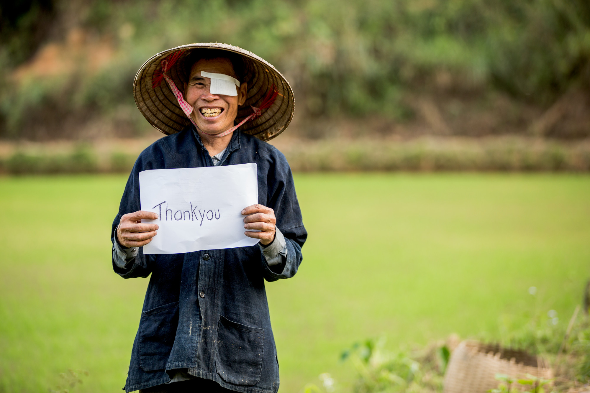 Khut in his field at home, wearing a hat and holding a Thank You sign.