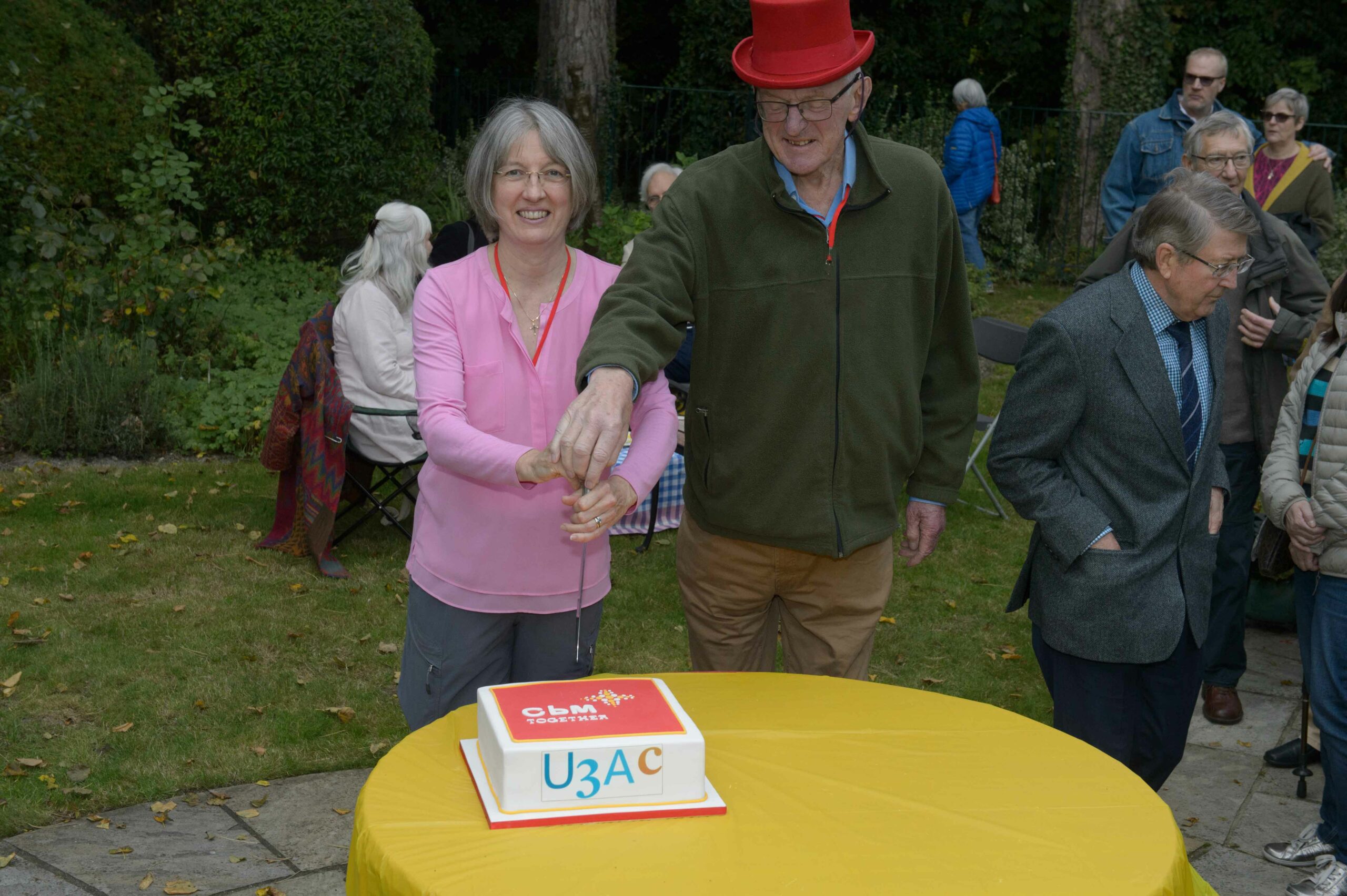 Gill and Peter Godber cutting the cake, with a CBM logo printed on
