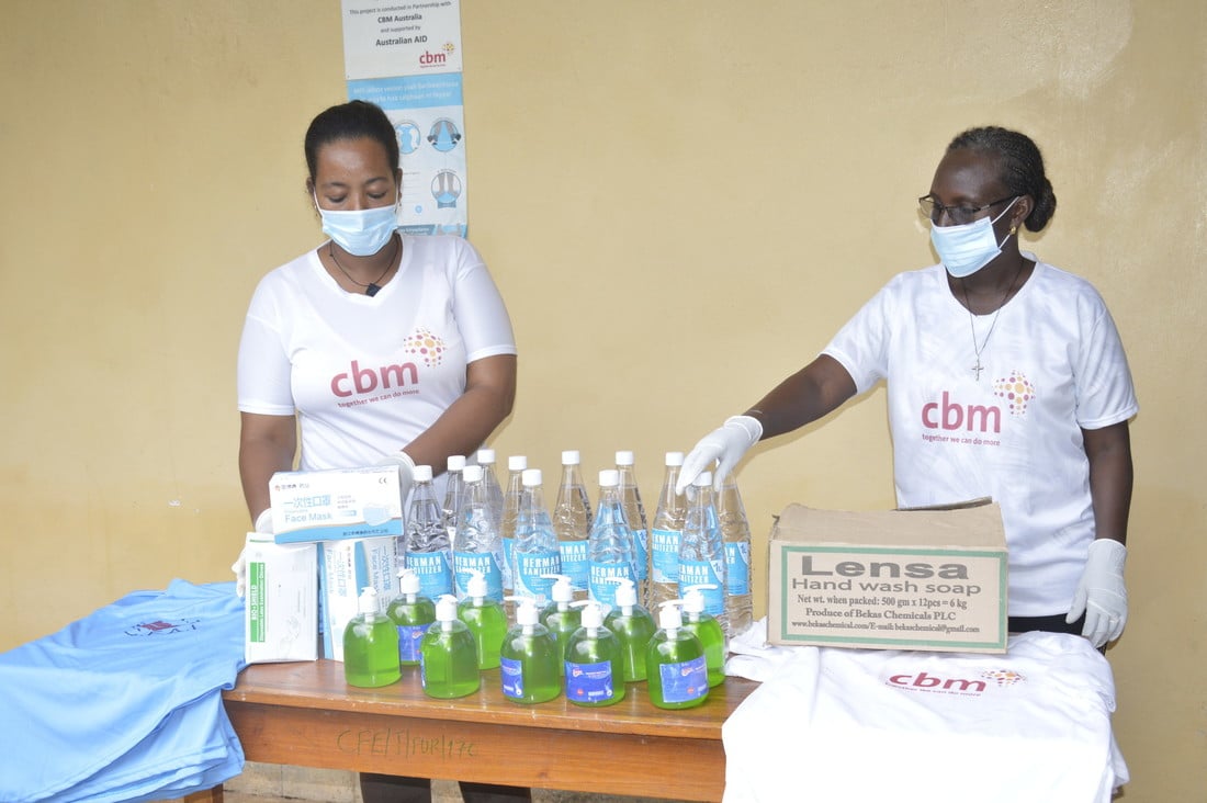 Two women wearing face masks and CBM t-shirts are counting out bottles of water and hand sanitiser