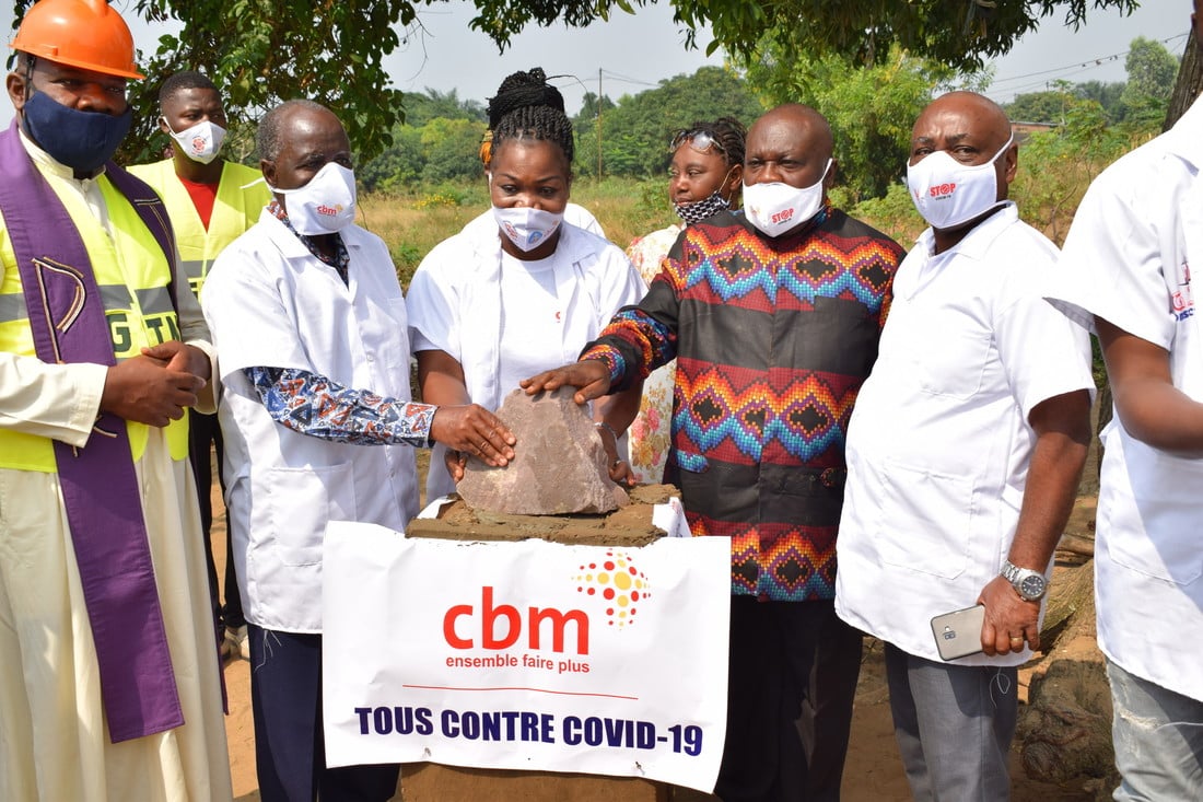 A group of people wearing face masks and all placing a hand on a piece of concrete in front of a CBM sign