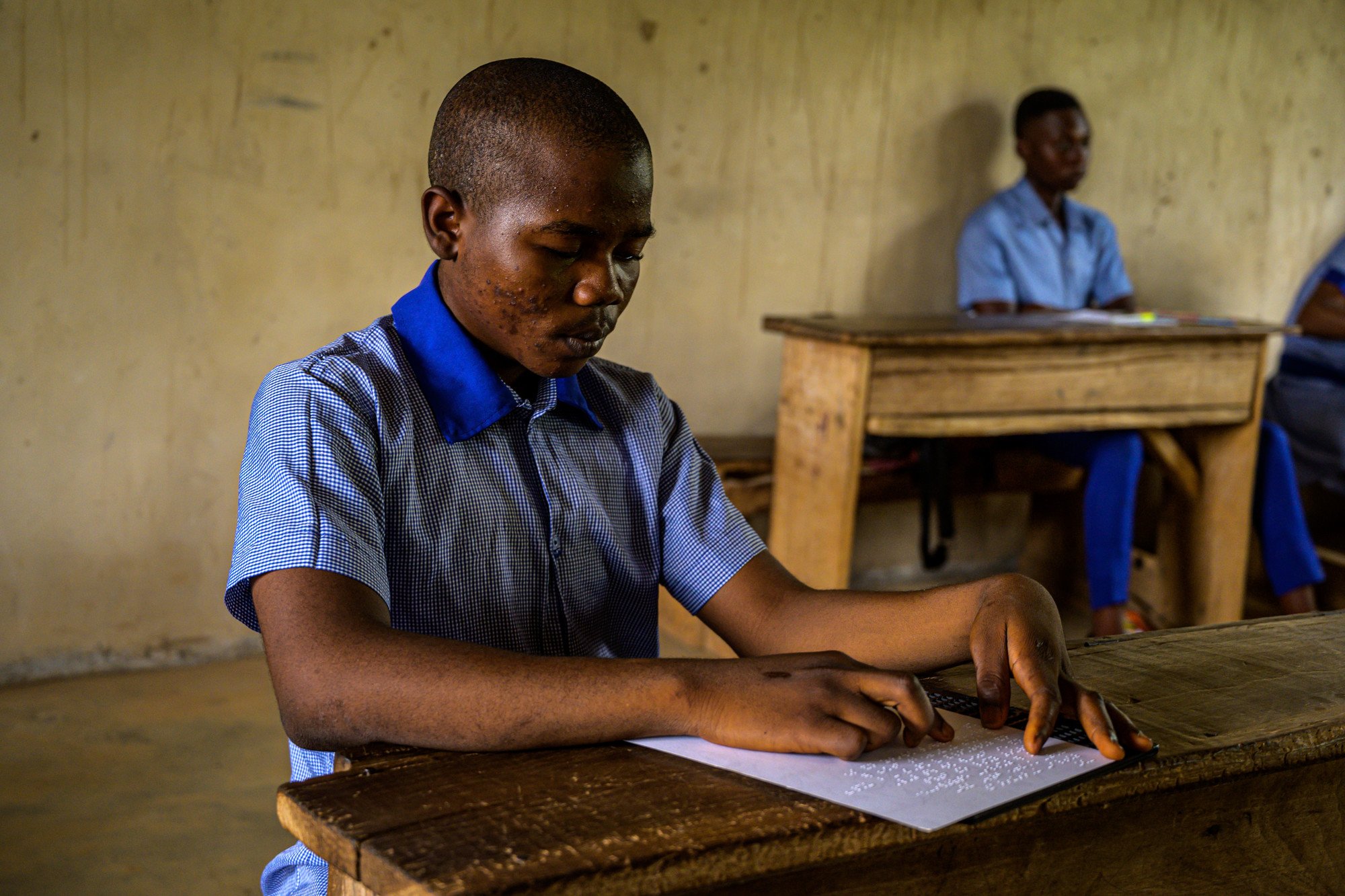 Male student, Possible, sat at a desk in his classroom and using Braille resources.
