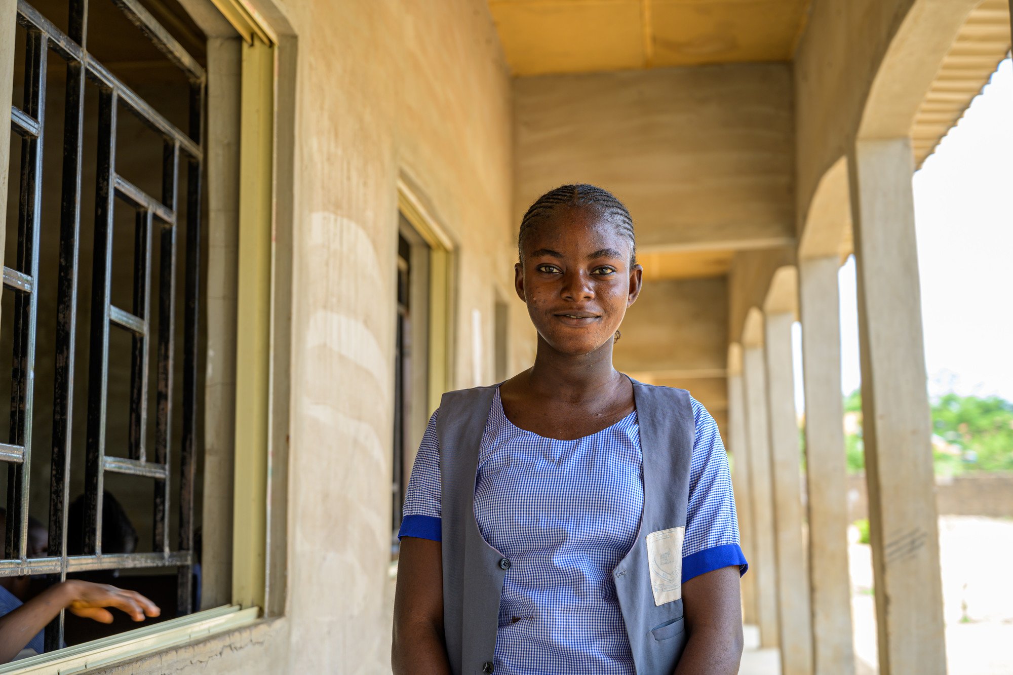 Female student, Rhoda, stood outside her school classroom and smiling.
