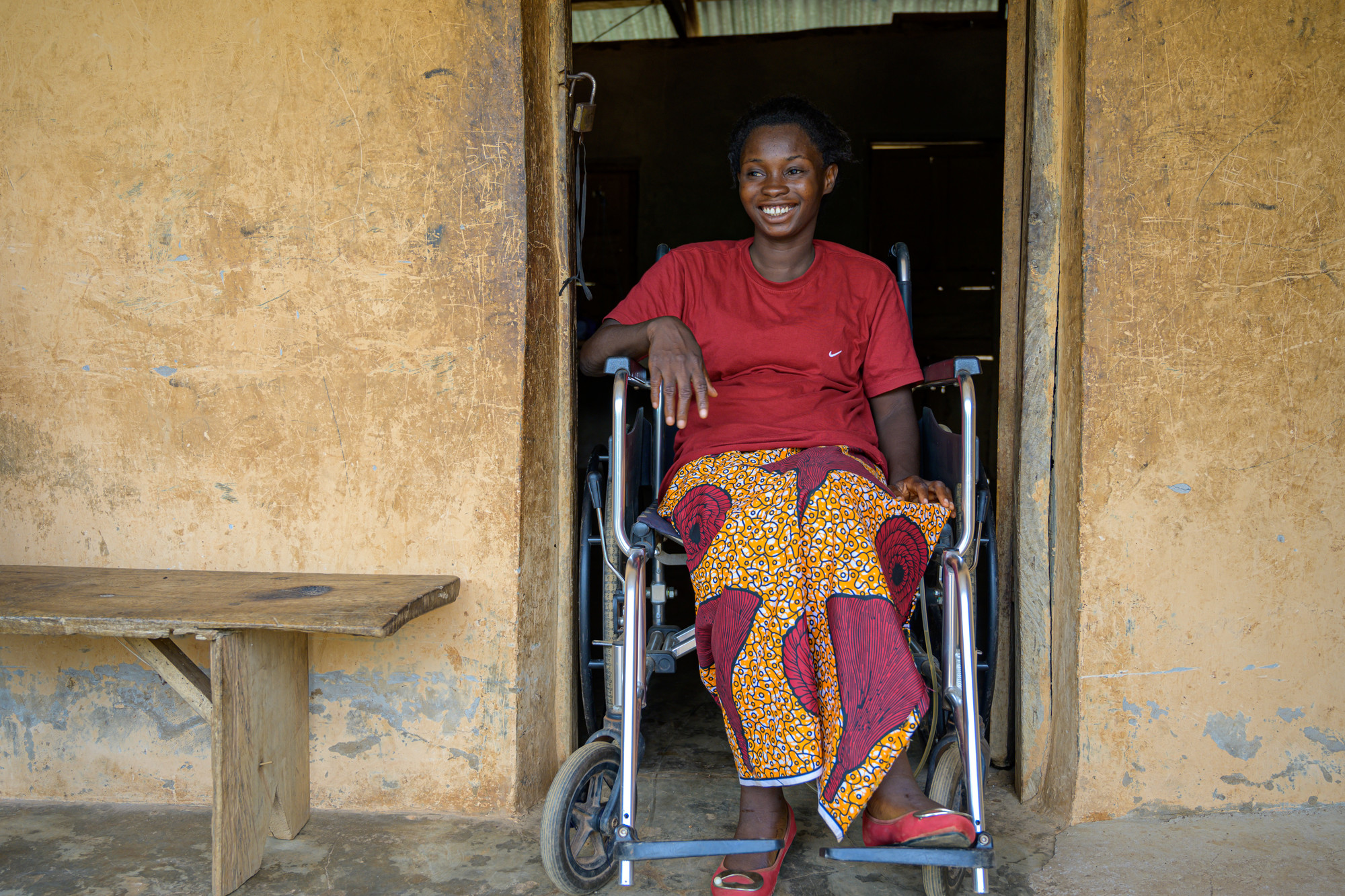 Wheelchair user, Blessing, in the doorway of her home, smiling.