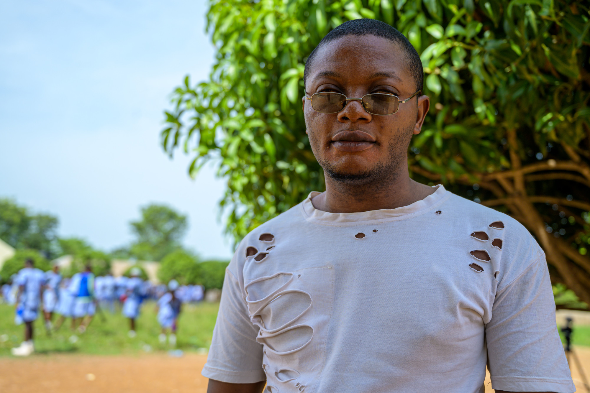 Teaching assistant, Ruben, standing outside, with school children in the background.