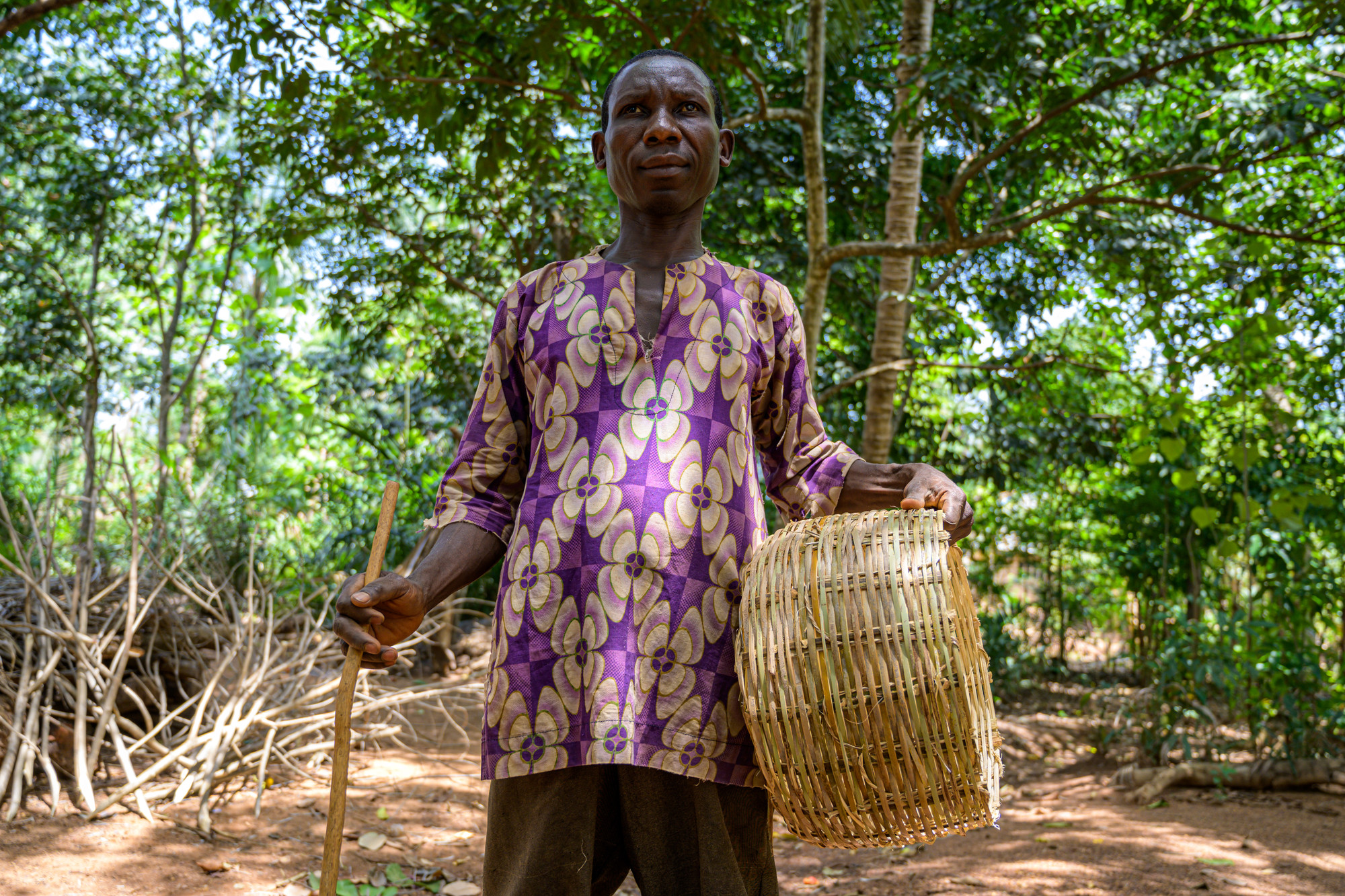 Job standing outside, holding a basket he's weaved.