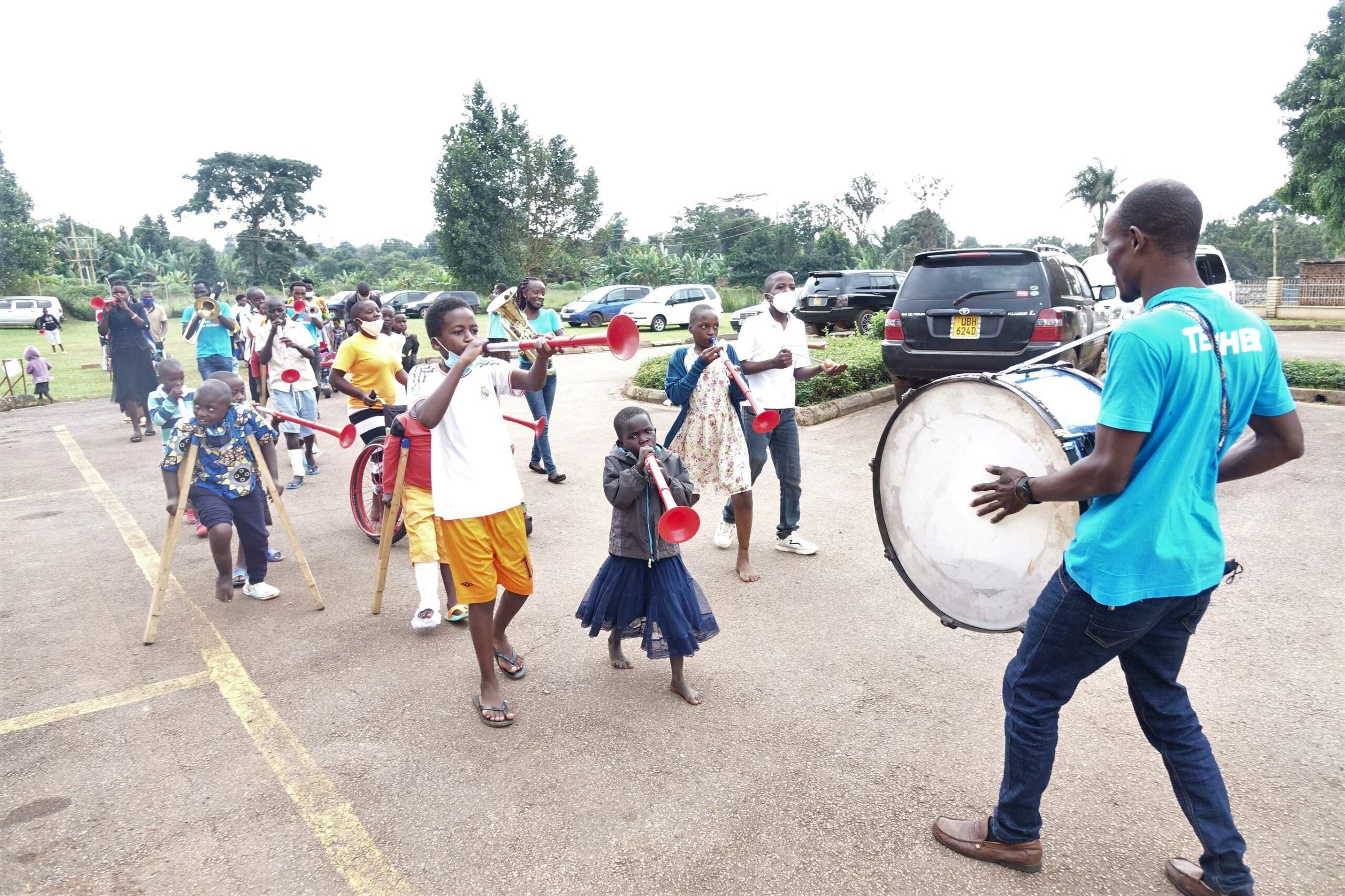 Children walking in a line through a car park, playing musical instruments .