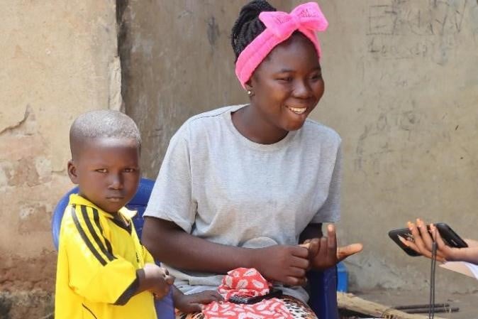 Faith sits, smiling, with her son by her side. 