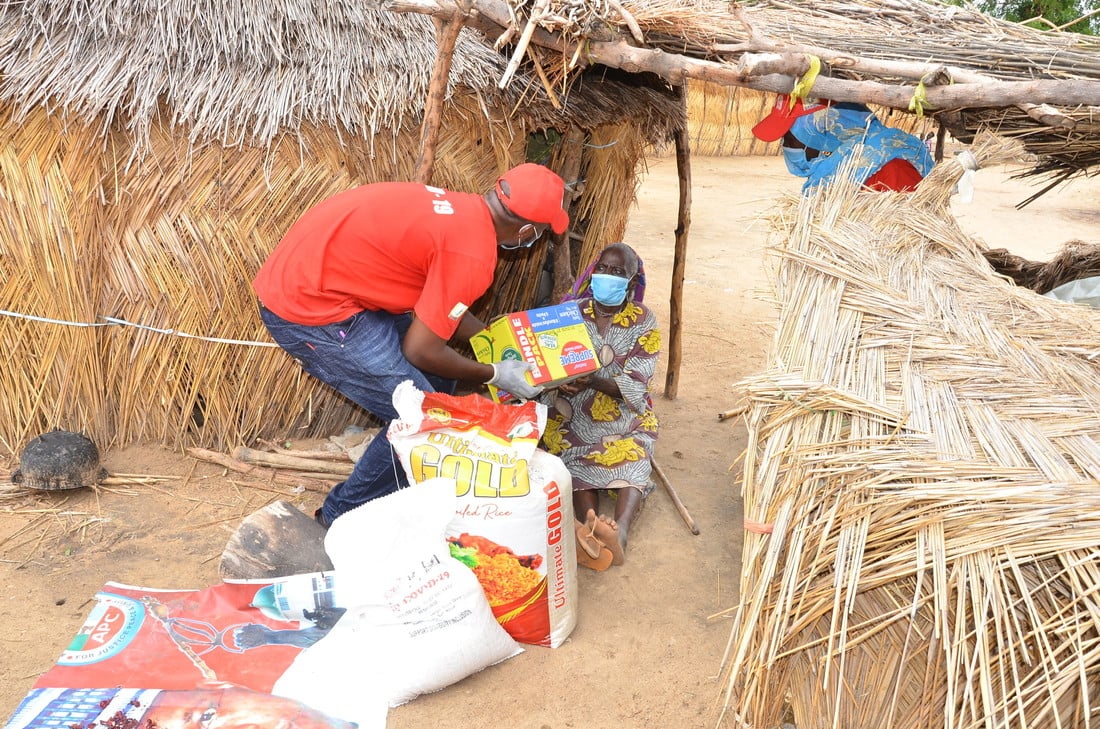 Male humanitarian worker hands emergency relief parcels to a an elderly women sat outside her home in rural Nigeria