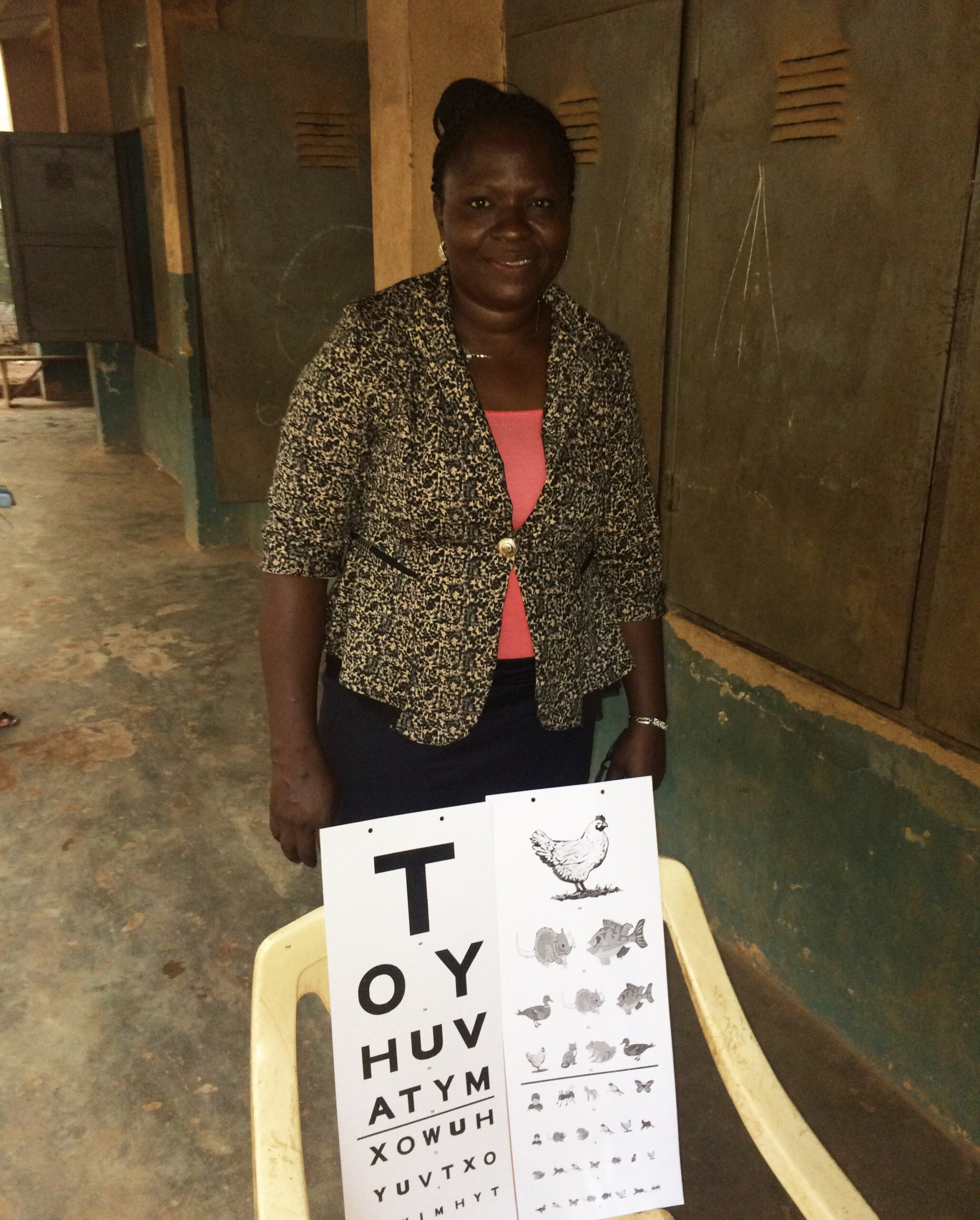 Mrs Aduke standing behind a chair with an eye chart on.