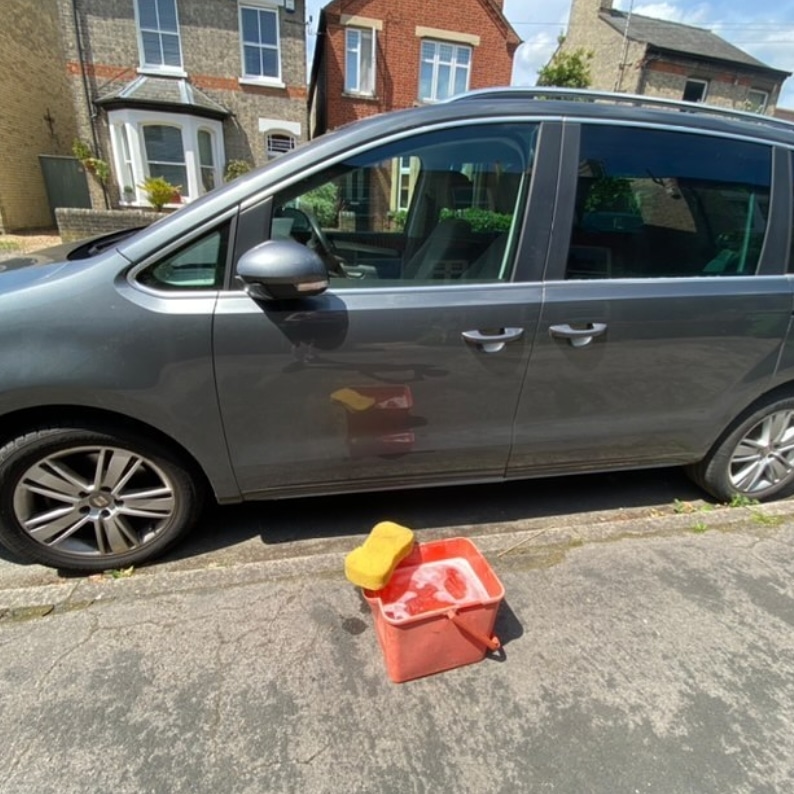 Car with a bucket of water and a sponge next to it.
