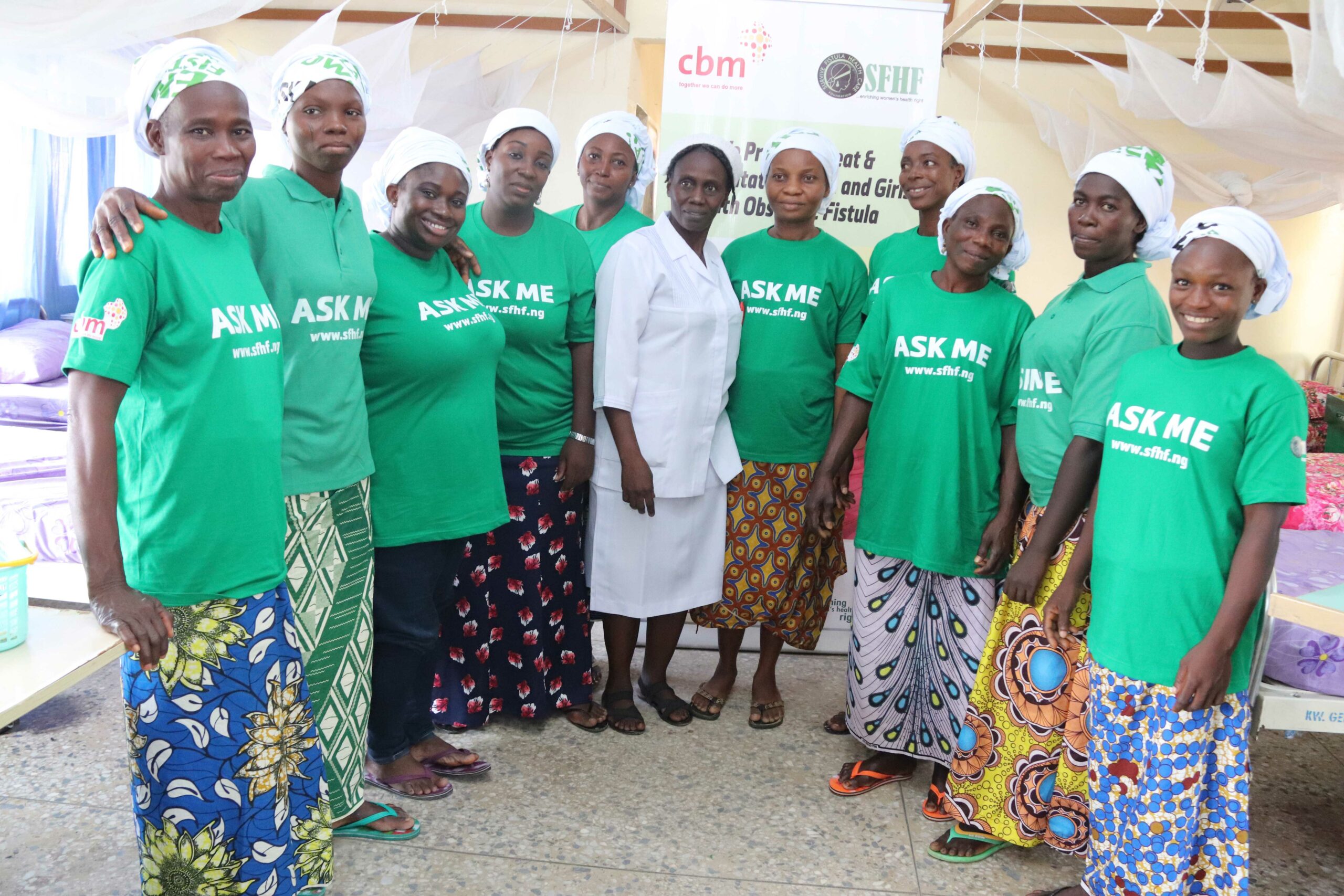 Women with lived experience of fistula who are now community champions, standing inside the Survive Fistula Healthcare Foundation hospital wing and wearing green t-shirts with ‘Ask me’ written on the front.