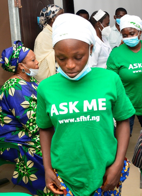 Justina wearing a mask and an 'Ask Me' green t-shirt 
