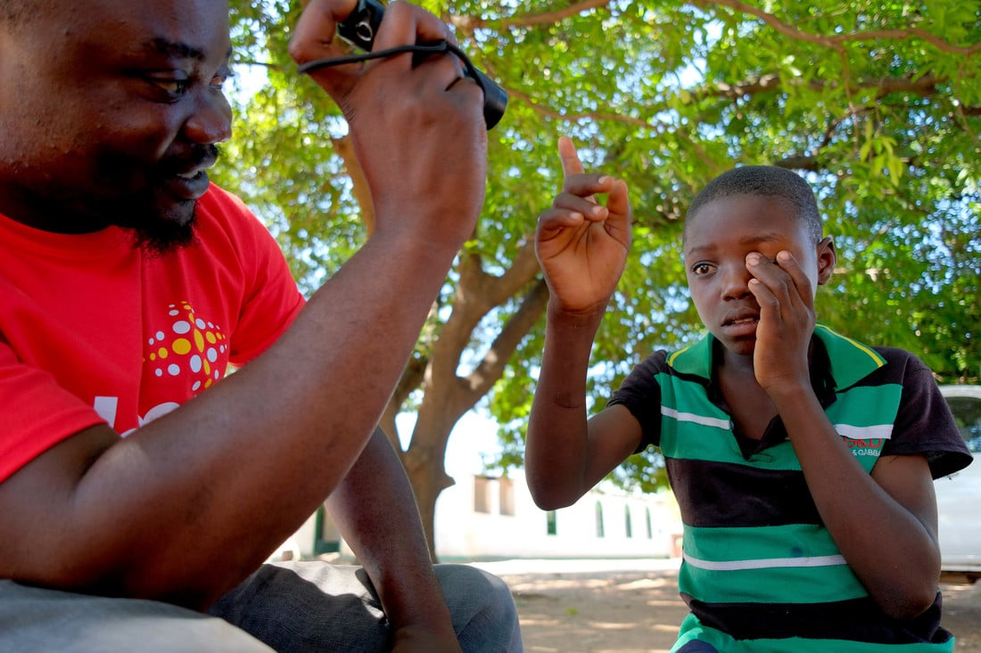 CBM health worker shining a torch in Jabes' right eye to examine it