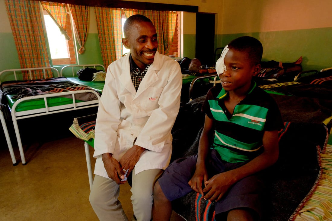 Jabes sat on a hospital bed with Dr Vincent Moyo, smiling.