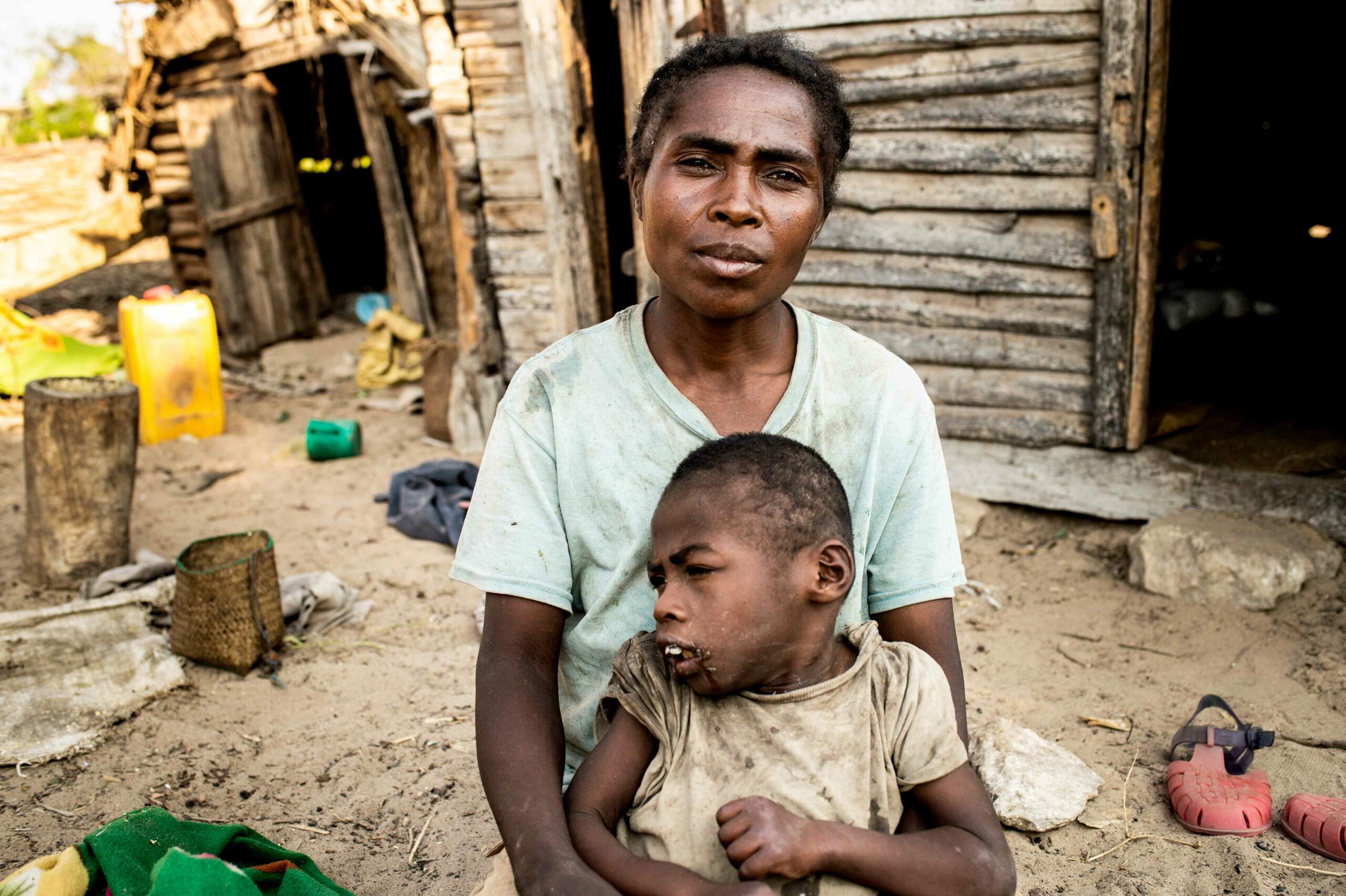 Women holds her son in front of their wooden hut