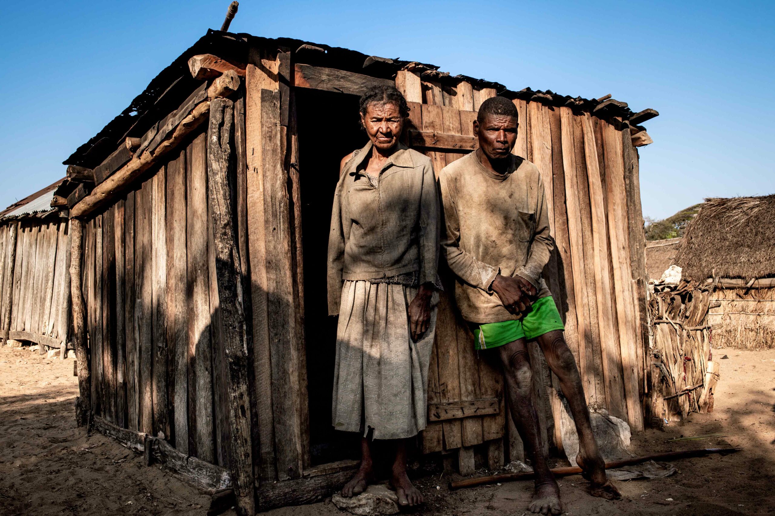 Mother and son stand outside their wooden hut