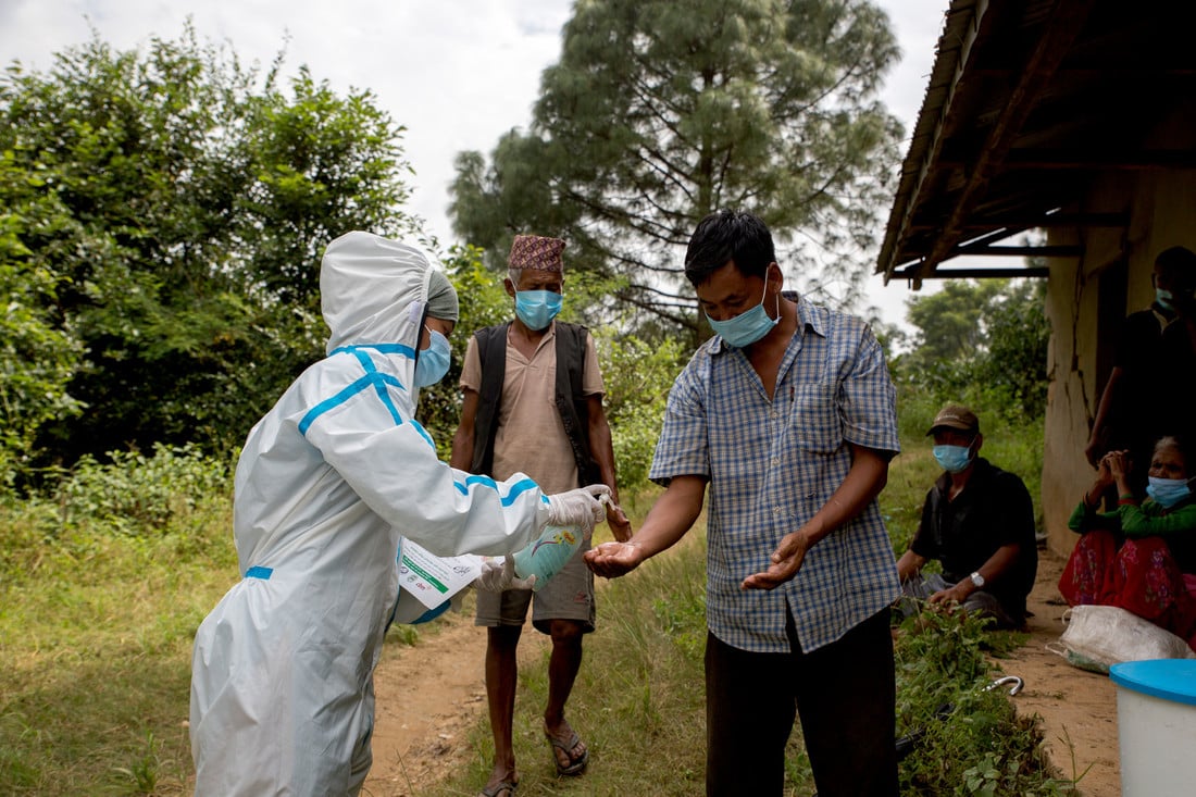 Female health worker in PPE handing out hand sanitiser to men in a rural village in Nepal