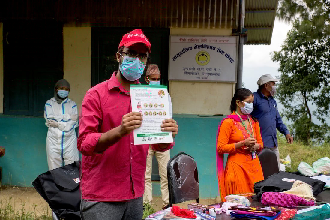 Man wearing a face mask and holding up a COVID-19 awareness brochure
