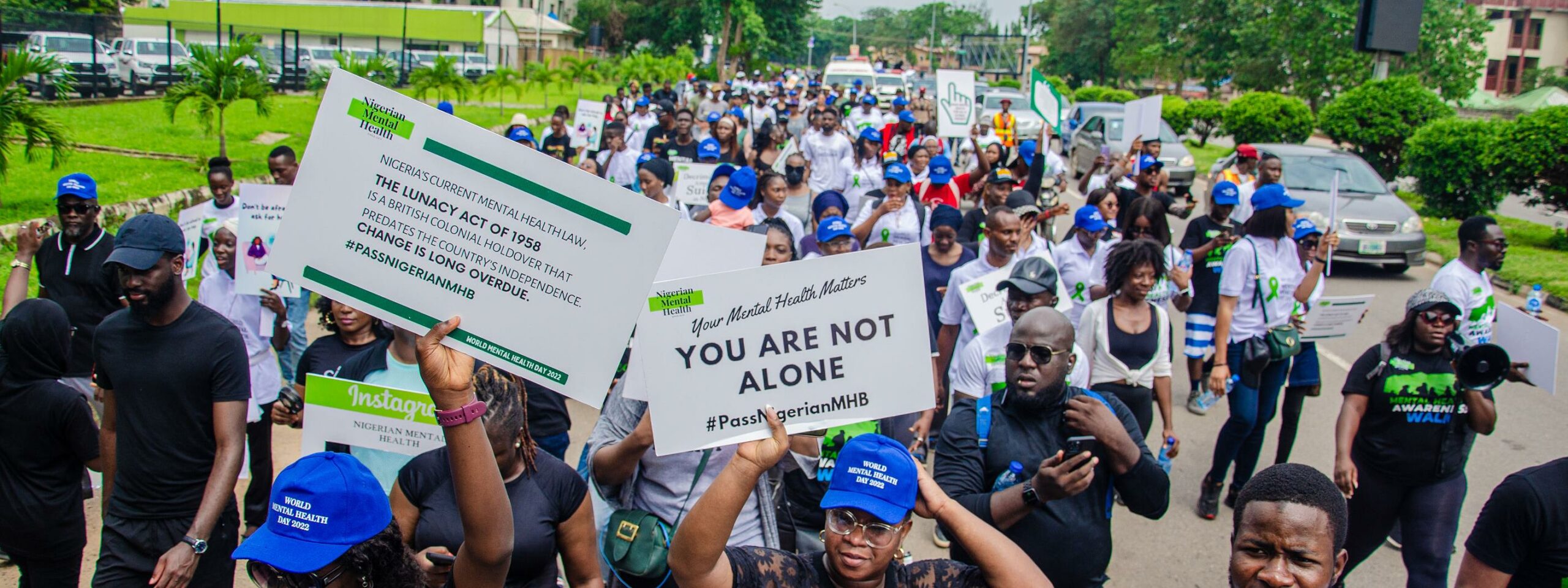 Many people walking together with banners showing positive mental health messages and #PassNigerianMHB