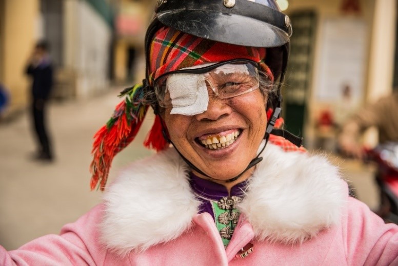 Pom from Vietnam, driving a motorcycle and smiling, with an eye patch over her right eye.