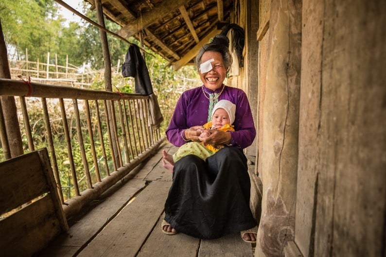 Pom sitting on her porch at home, holding her baby grandson