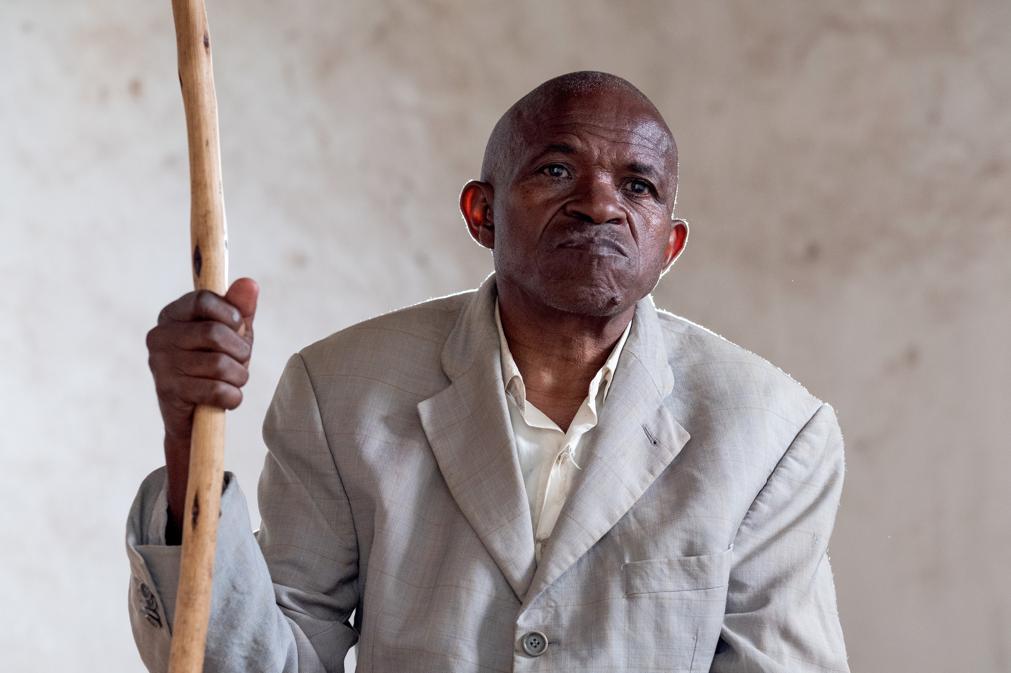 Jean-Baptiste sitting in his home home his walking stick