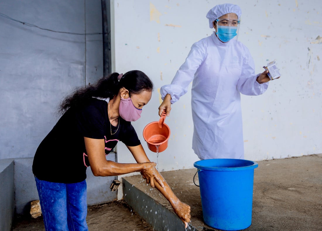 Female health worker in PPE pouring water onto a lady's arms and hands