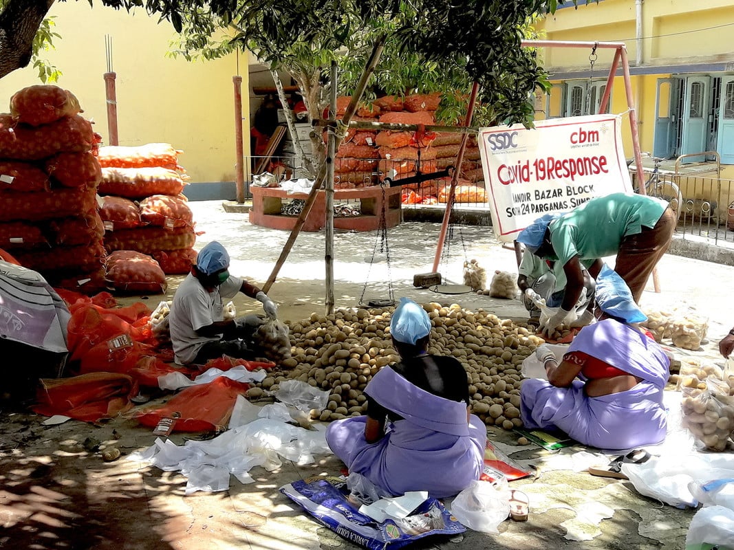 Humanitarian workers sat on the floor packaging potatoes into bags, wearing PPE