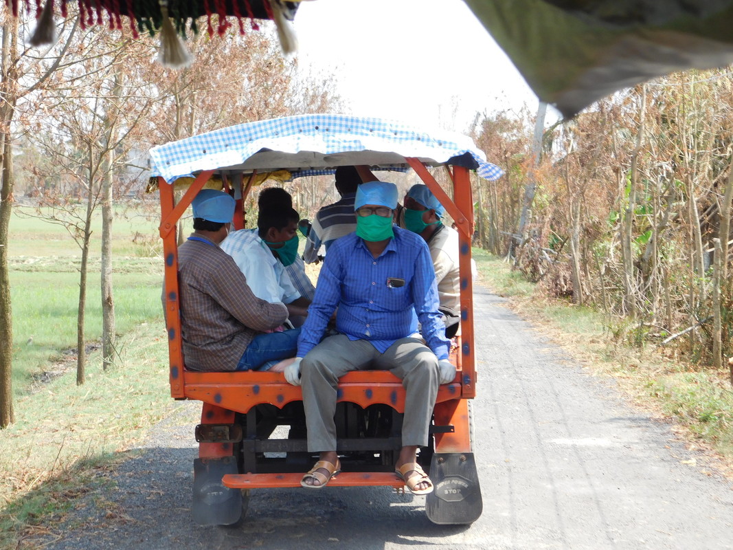 Humanitarian workers sitting in PPE in an open tuk tuk, driving along the road