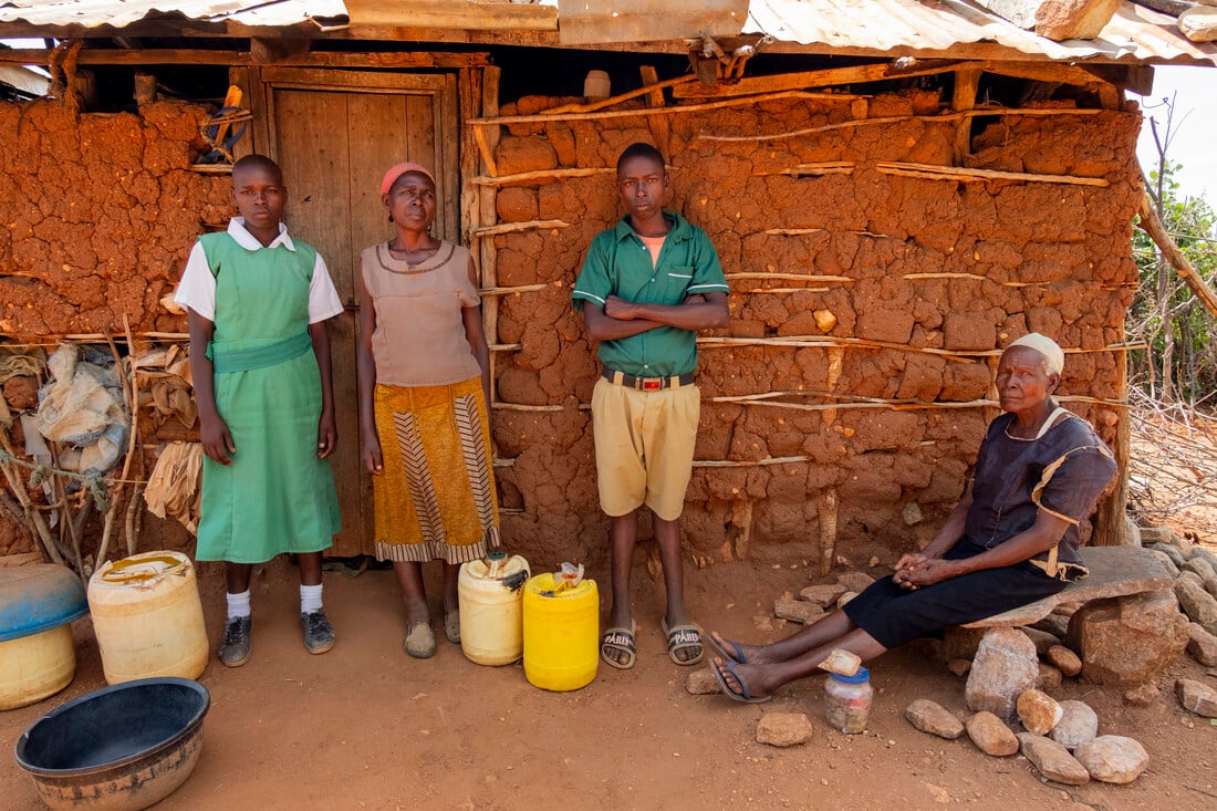Sofia standing with her grandchildren against her mud hut.