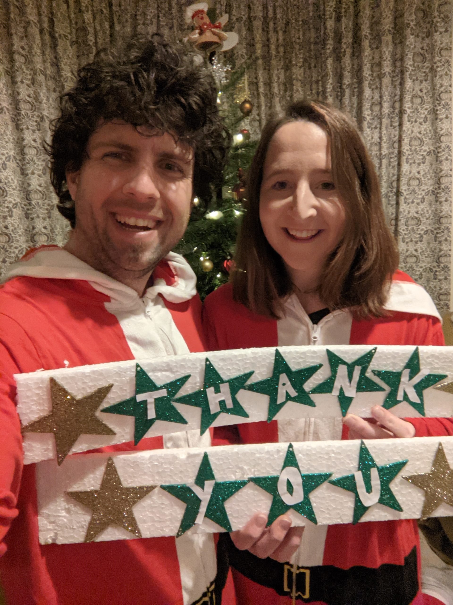 Steph and her husband Brock, in santa outfits and holding a Thank You sign
