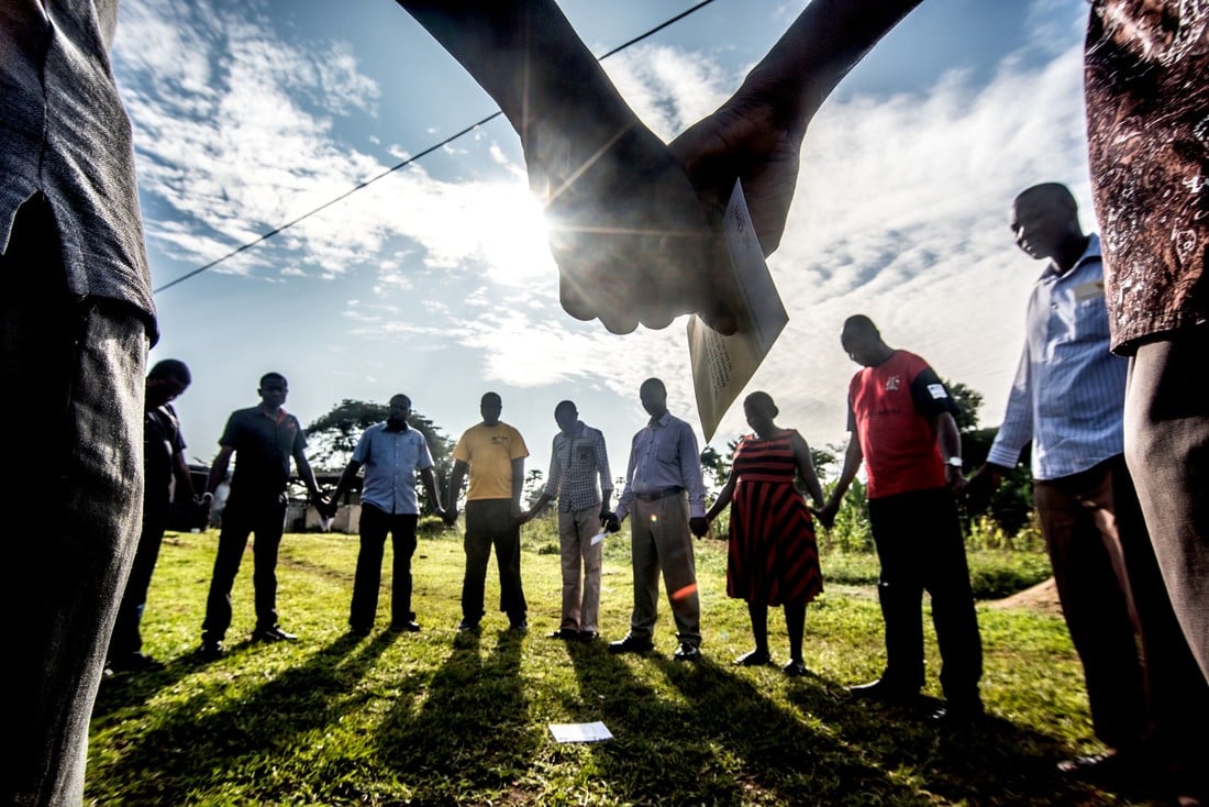 CBM staff and partners holding hands and praying together in Uganda