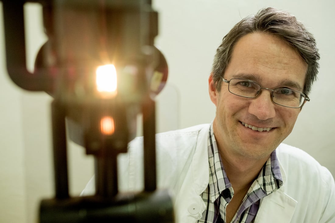 Dr Heiko Philippin sat next to a laser machine, smiling.