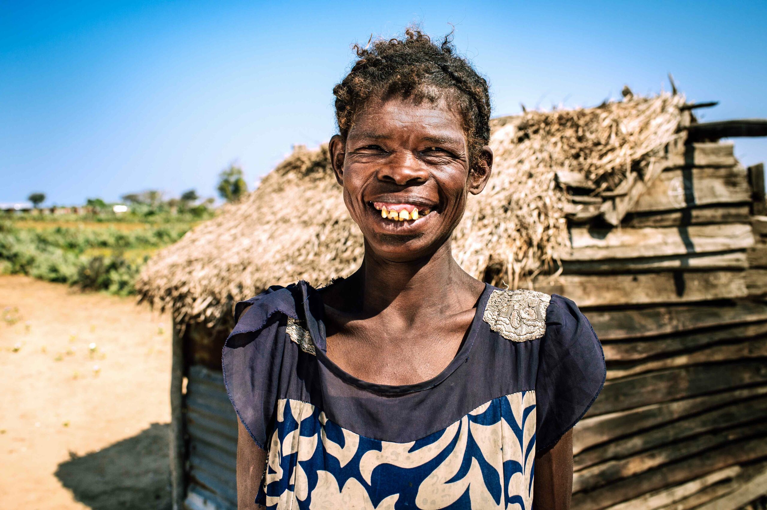 Women with a big smile on her face, standing in front of her wooden hut