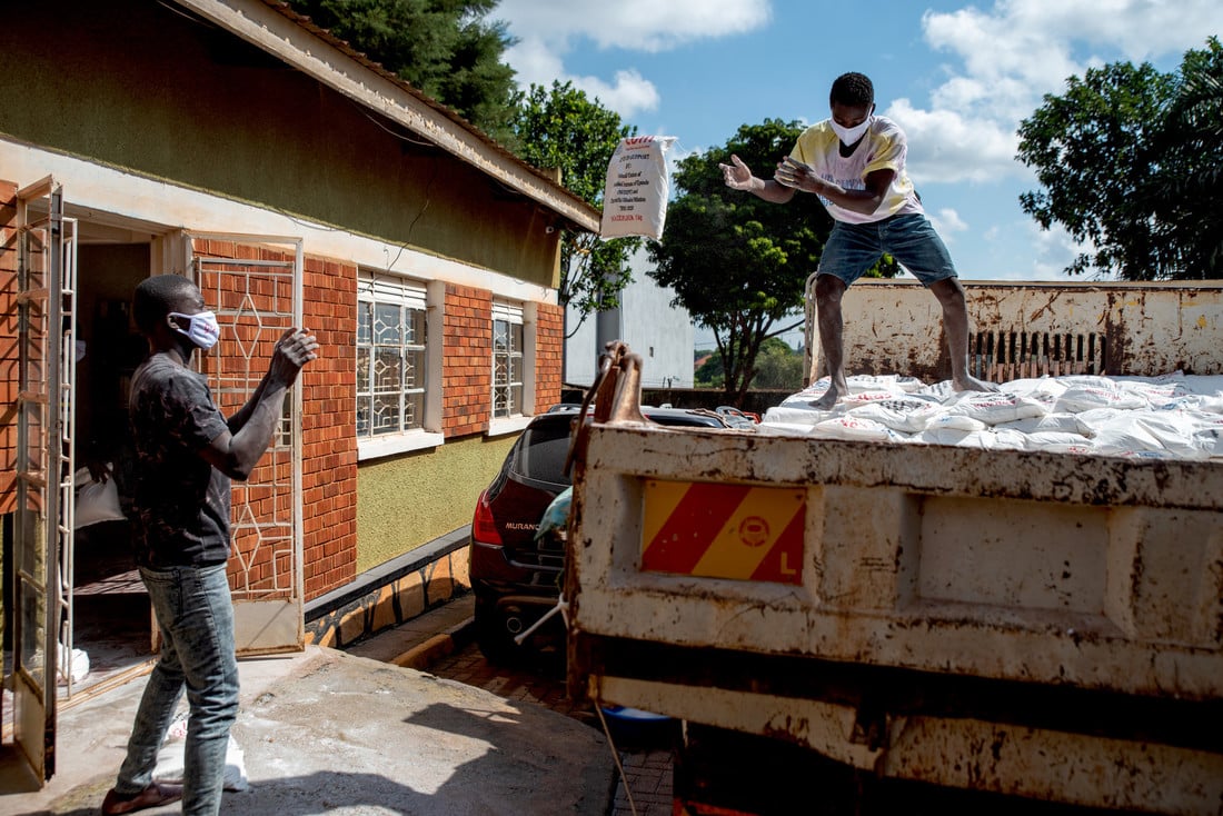 Man standing on top of a truck, throwing a food package to another man standing on the ground