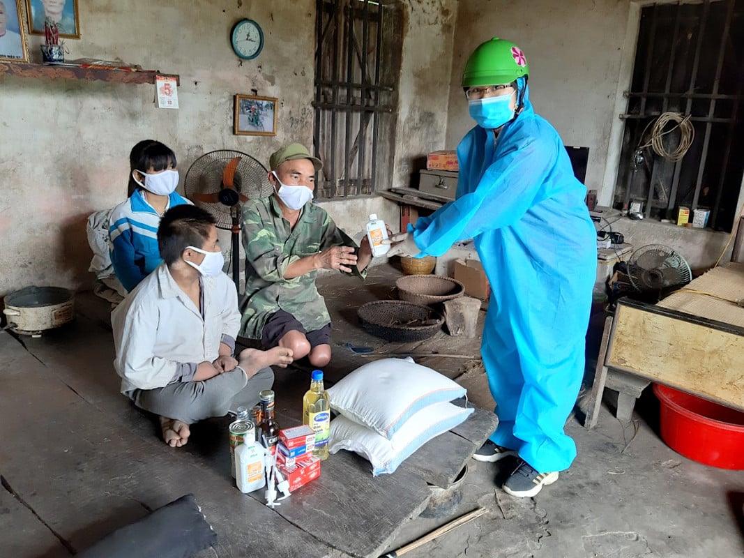 Female humanitarian worker wearing full PPE handing 3 family members some relief packages, inside their home in Vietnam