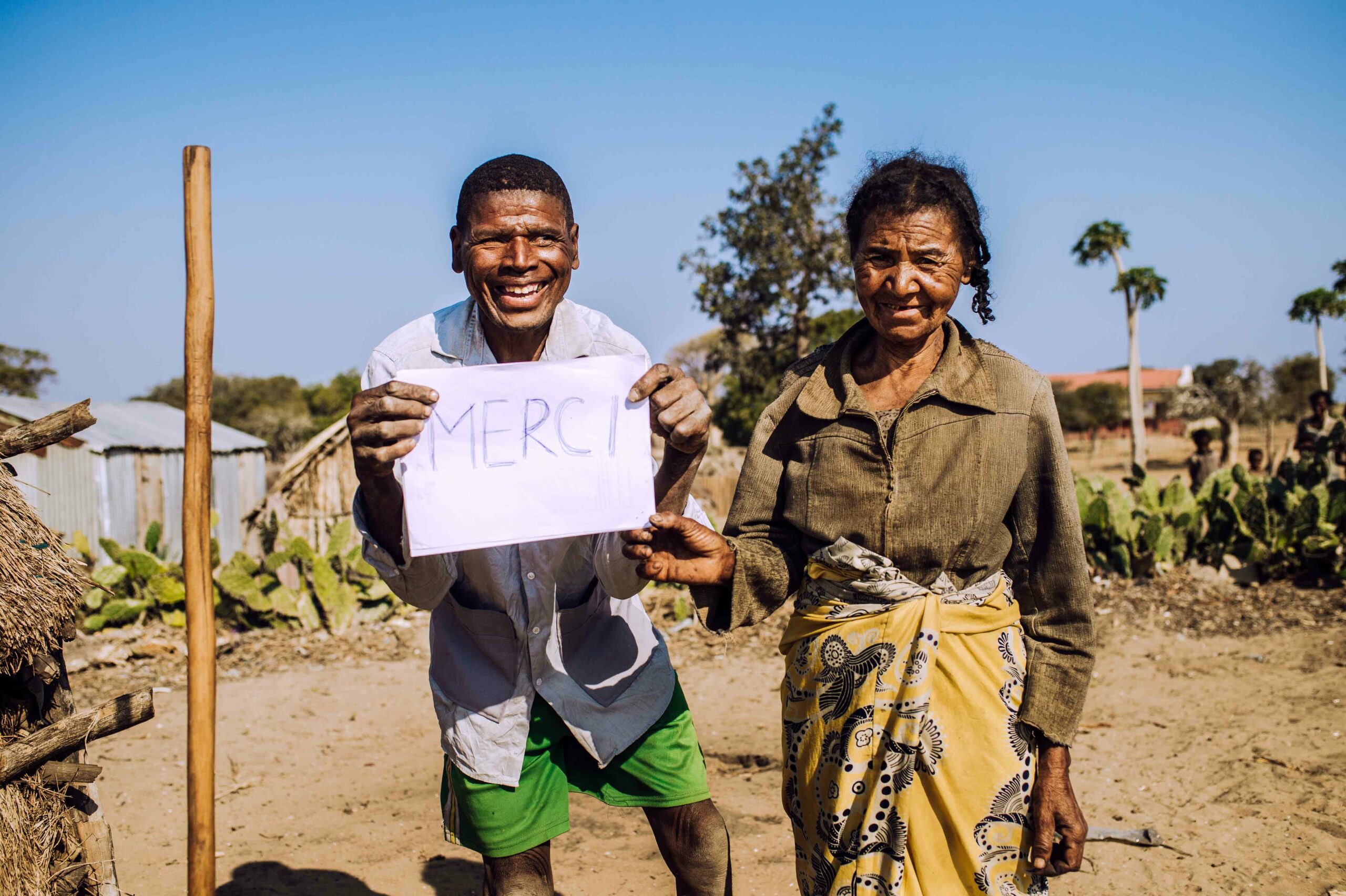 Young adult male holding a sign saying ‘Thank You’ in French, standing next to older women.