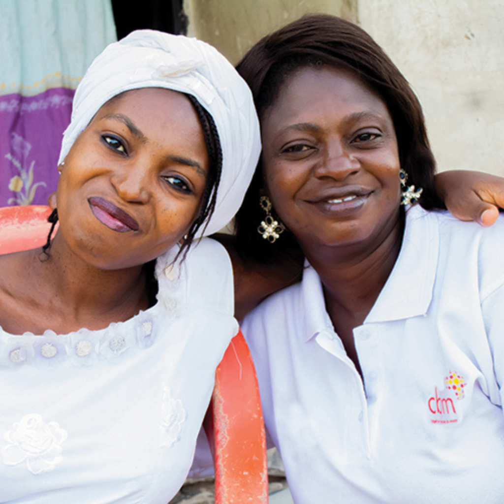 Maimunat, wearing white puts her arm around Victoria, who is wearing a cbm shirt.