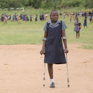 A girl with an amputated leg stands on crutches in a school playing field