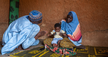A baby sits on their mum's knee as a doctor kneels forwards and examines their eyes.