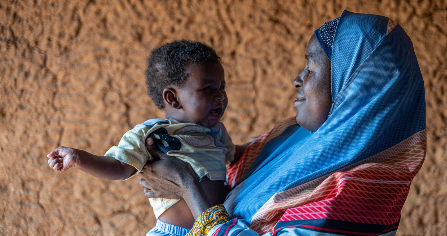 A baby is held by their mother who looks at them with a smile.
